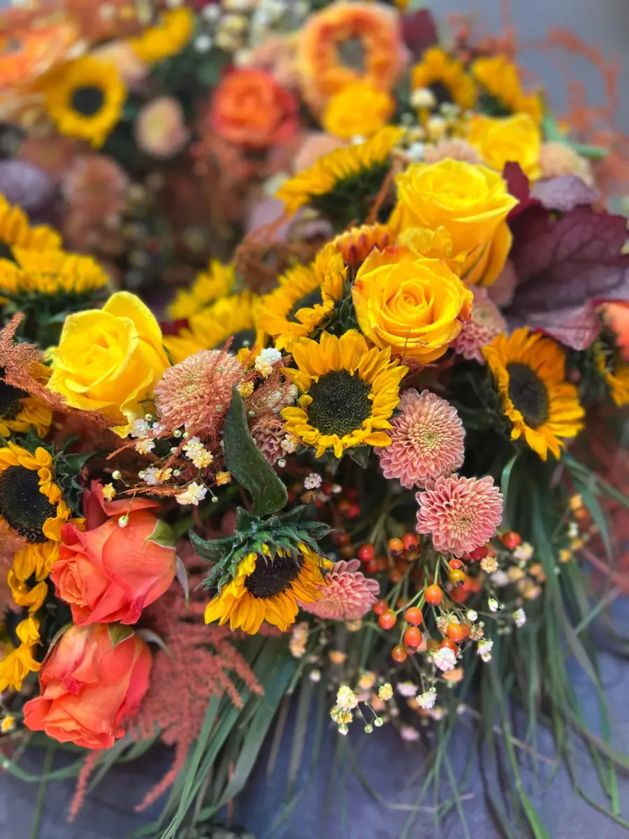 Trauergesteck in Gelb und Orange mit Sonnenblumen, Rosen und Hagebutten